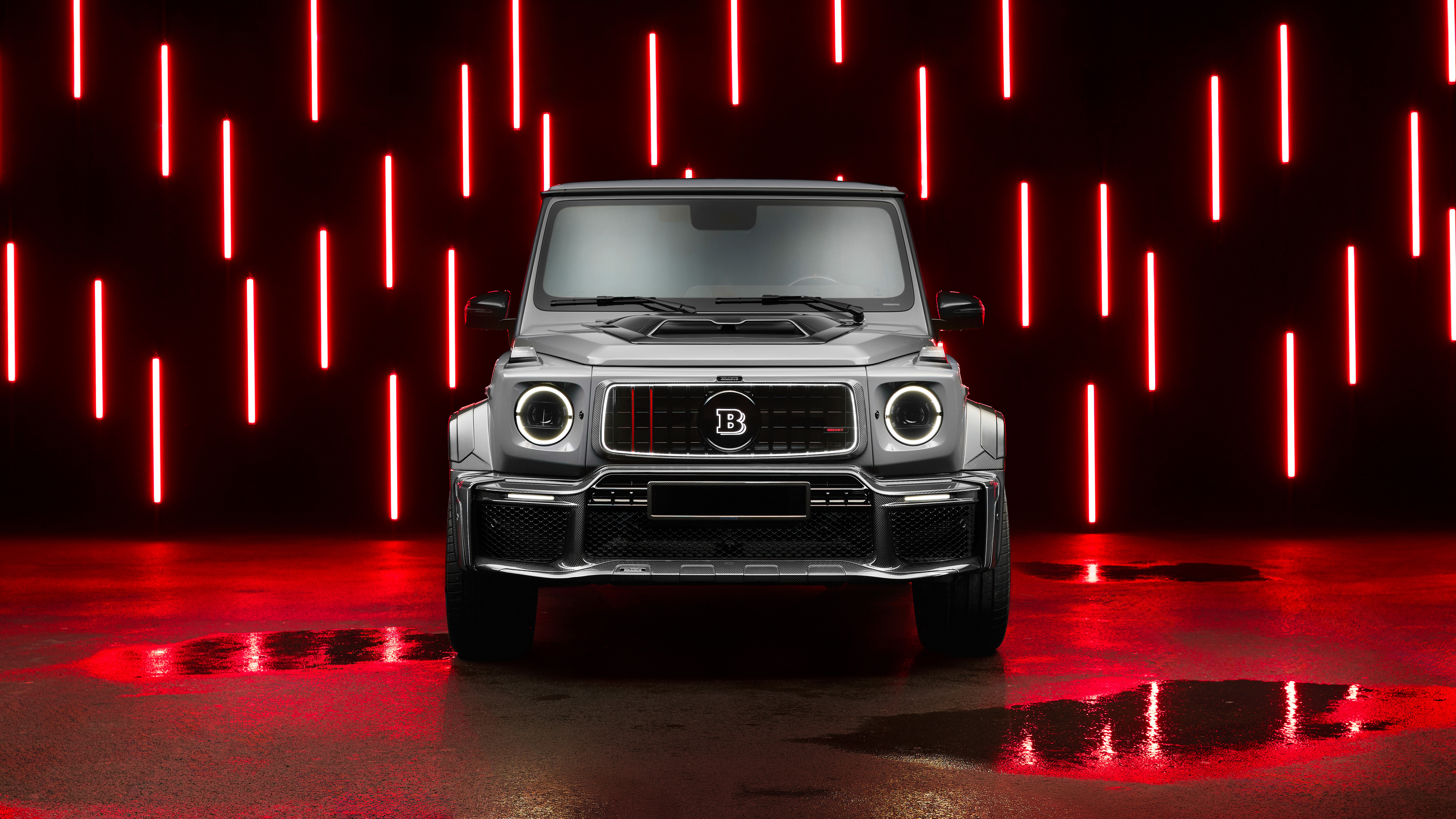 Front view of a metallic silver luxury SUV parked in a dark room illuminated by vertical red neon light bars reflecting off the ground.