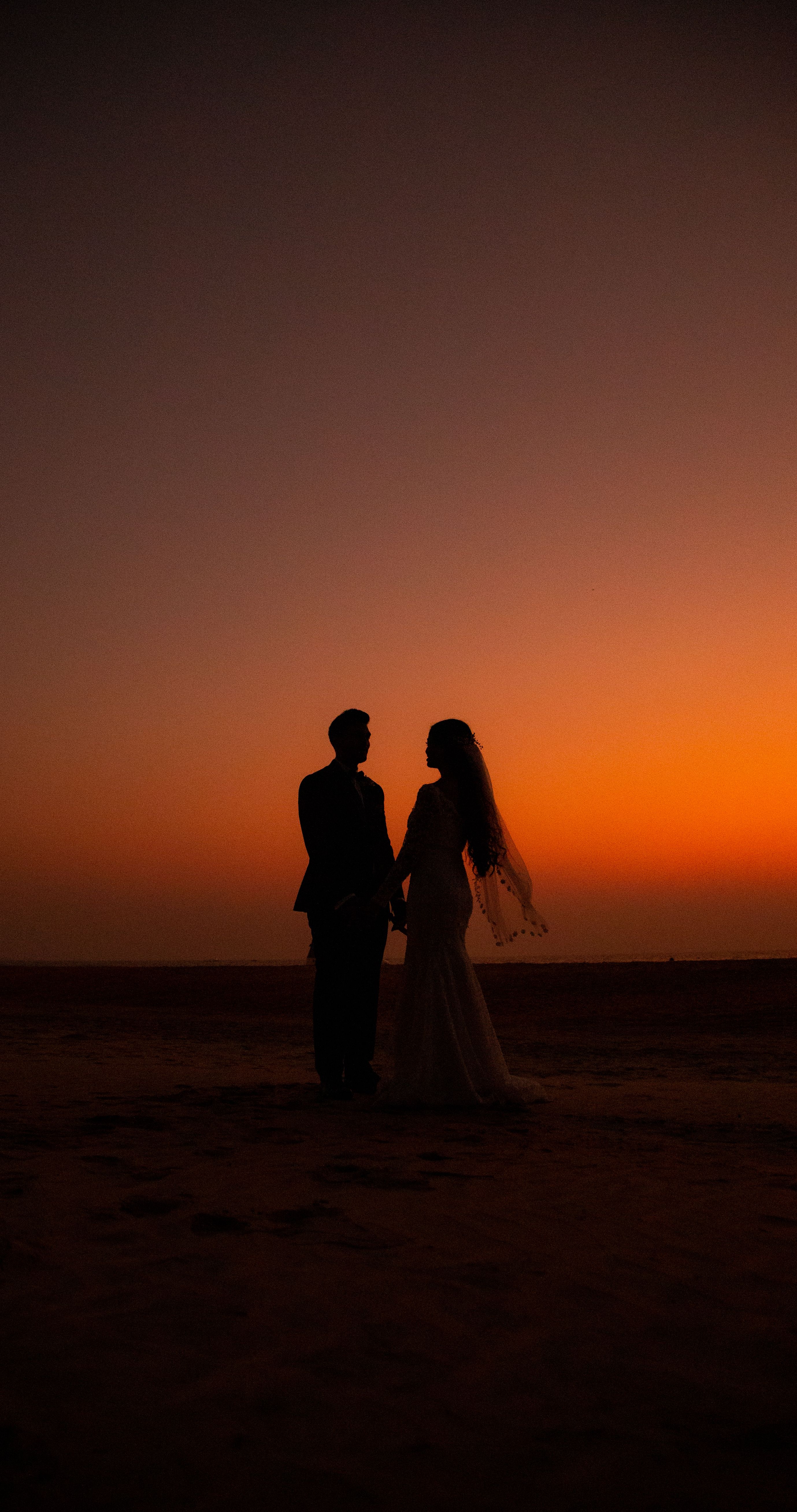 Silhouette of a couple holding hands on a beach at sunset, capturing love and ro
