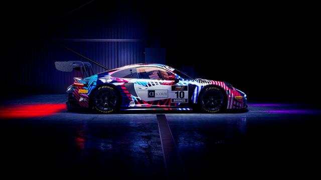 Side view of a race car featuring a bold colorful livery parked in a dark garage with neon reflections.
