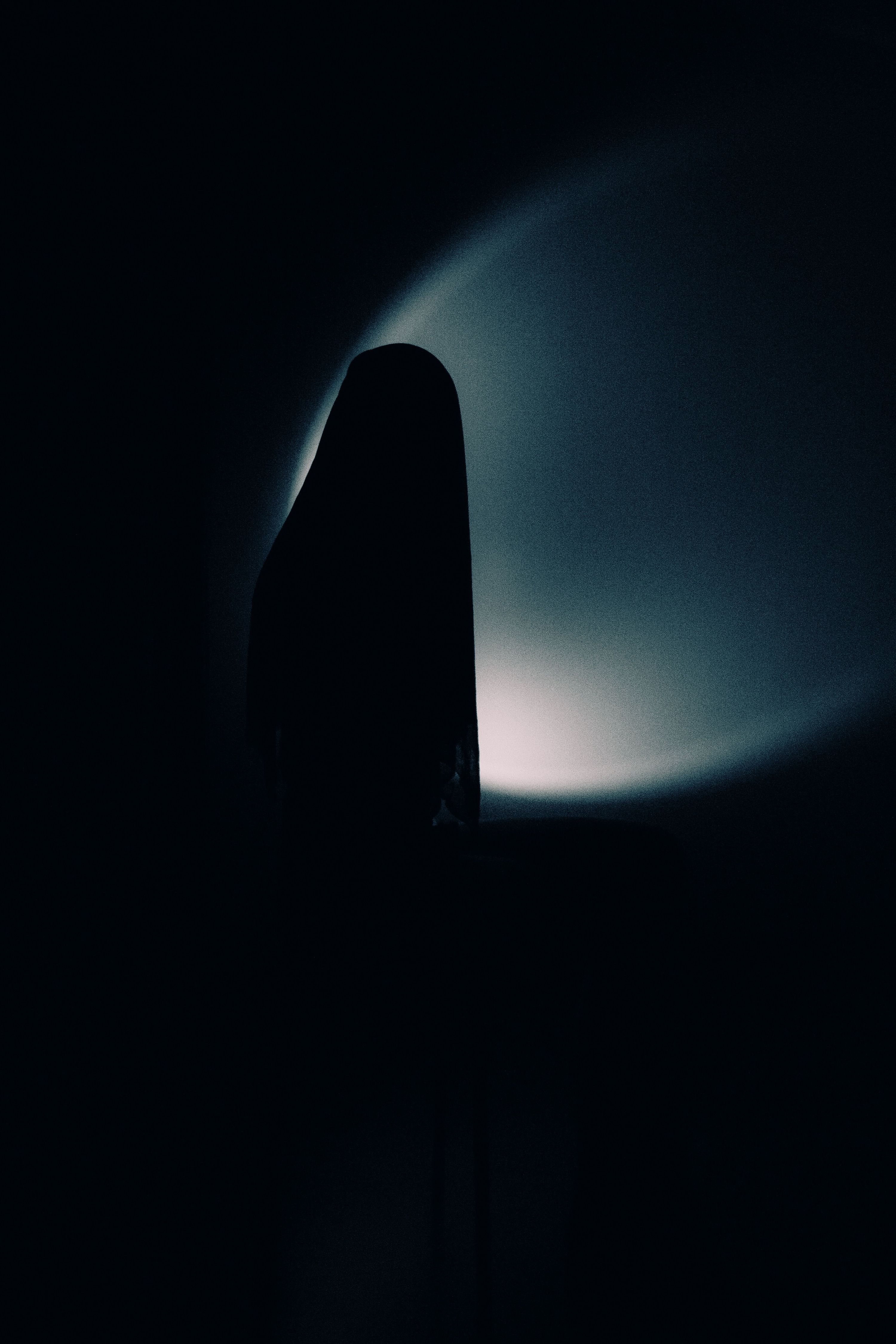 A dark silhouette of a figure against a moody, shadowy background.