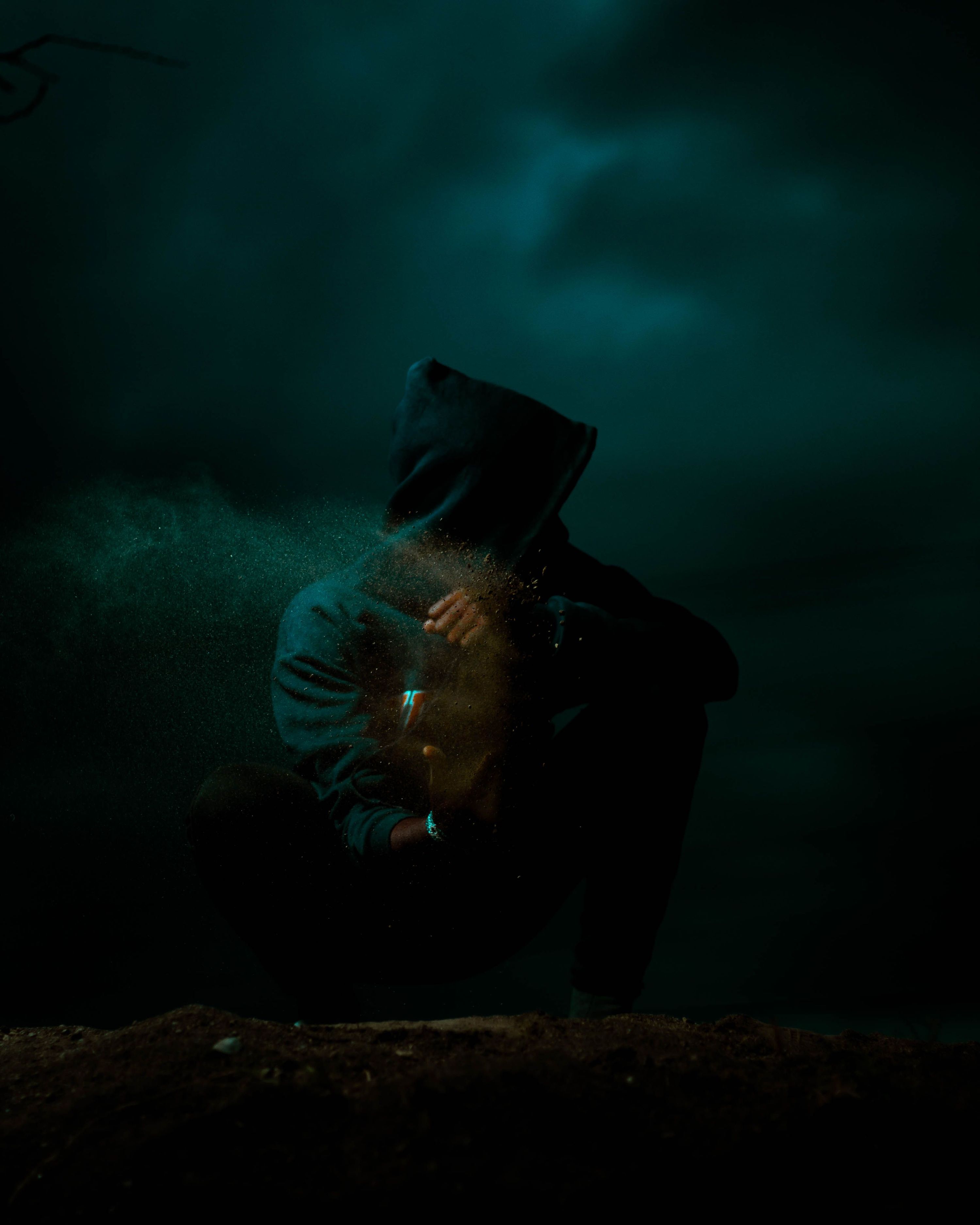 A solitary hooded figure in a dark, mysterious setting with powder scattering an