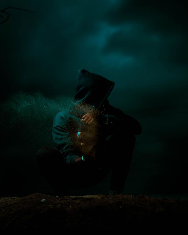 A solitary hooded figure in a dark, mysterious setting with powder scattering an