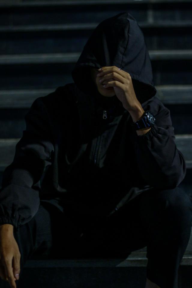 A man in a dark hoodie sitting on steps at night, creating a mysterious urban vi