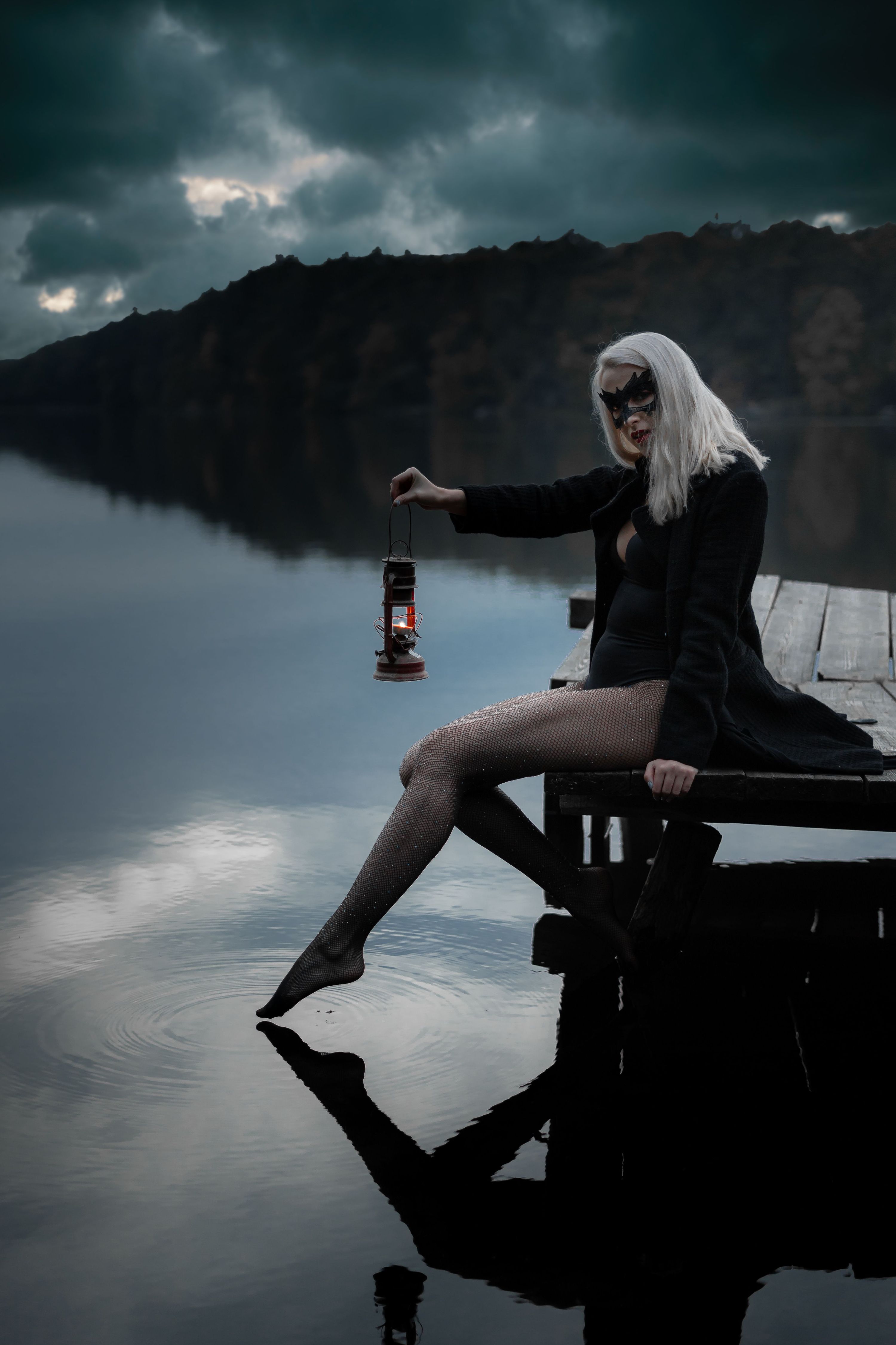 Side view of blond female in trendy apparel and decorative mask reflecting in ri